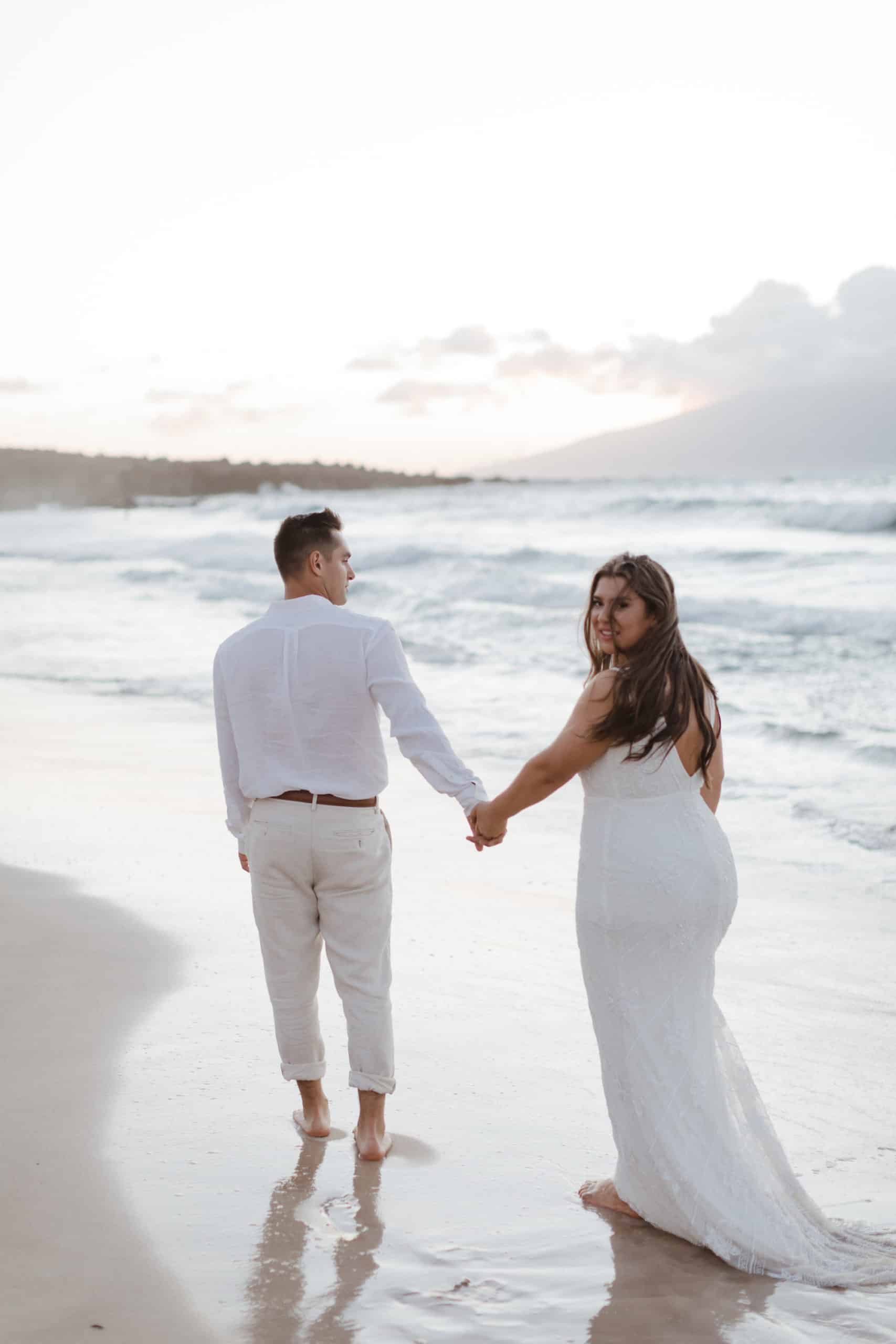 A couple is holding hands on the beach during their elopement in Maui.