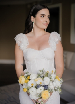 Woman in white dress holding a bouquet of yellow and white flowers, standing indoors.