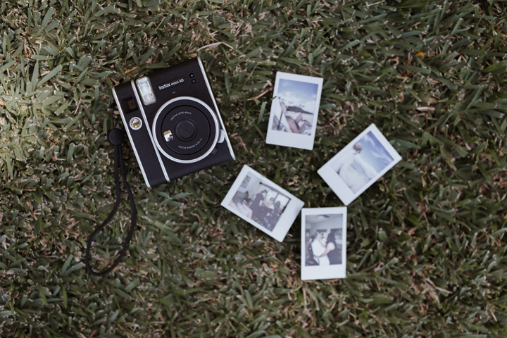 A black instant camera on grass next to four developed instant photos.