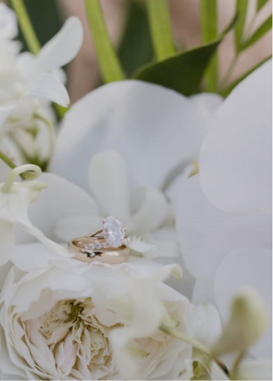 A gold ring set with a sparkling gemstone is nestled in a bouquet of white flowers.