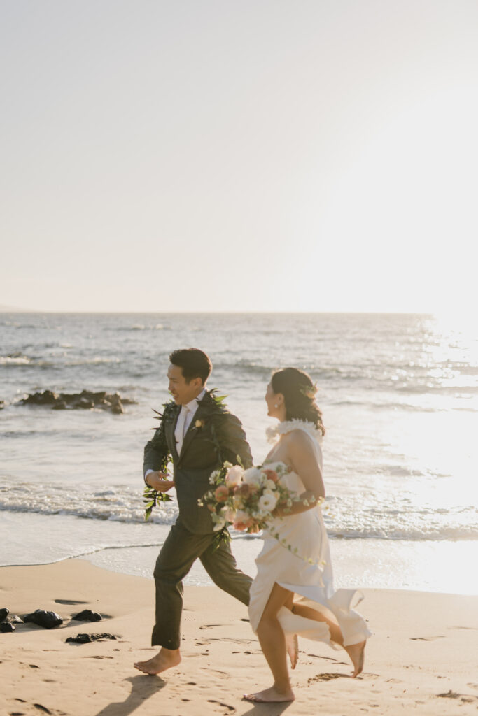 Roam Elopements, Maui Elopements, Happy couple running on beach in wedding attire.