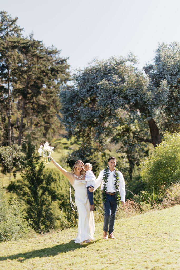 Roam Elopements, Maui Elopements, Happy family elopement: Bride, groom, and child walk on lawn.