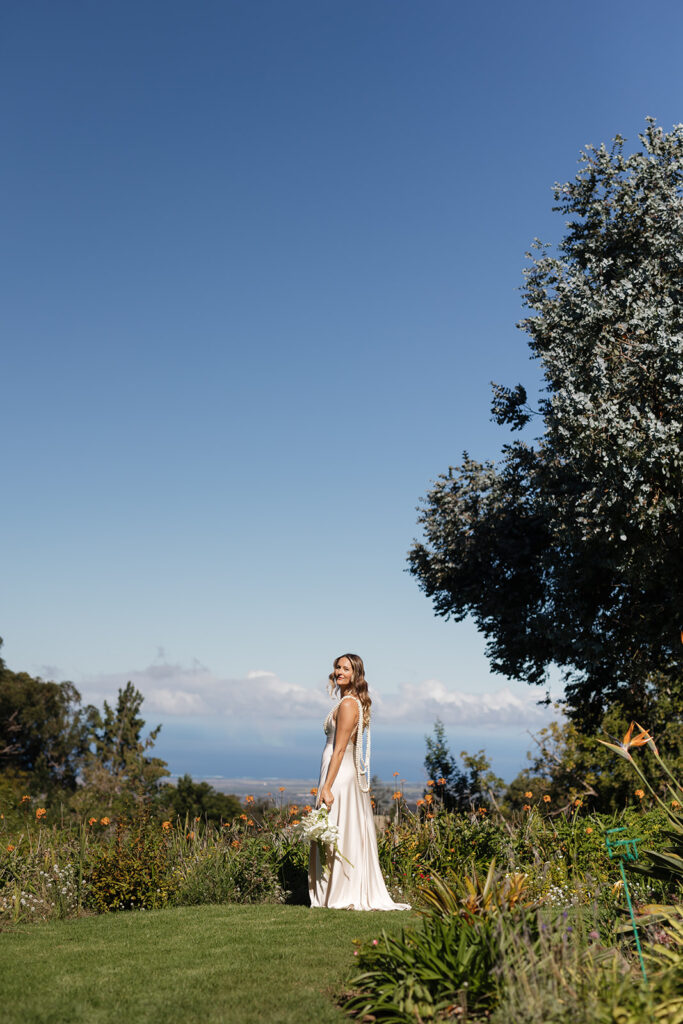 Roam Elopements, Maui Elopements, Bride in elegant dress in garden setting with blue sky.