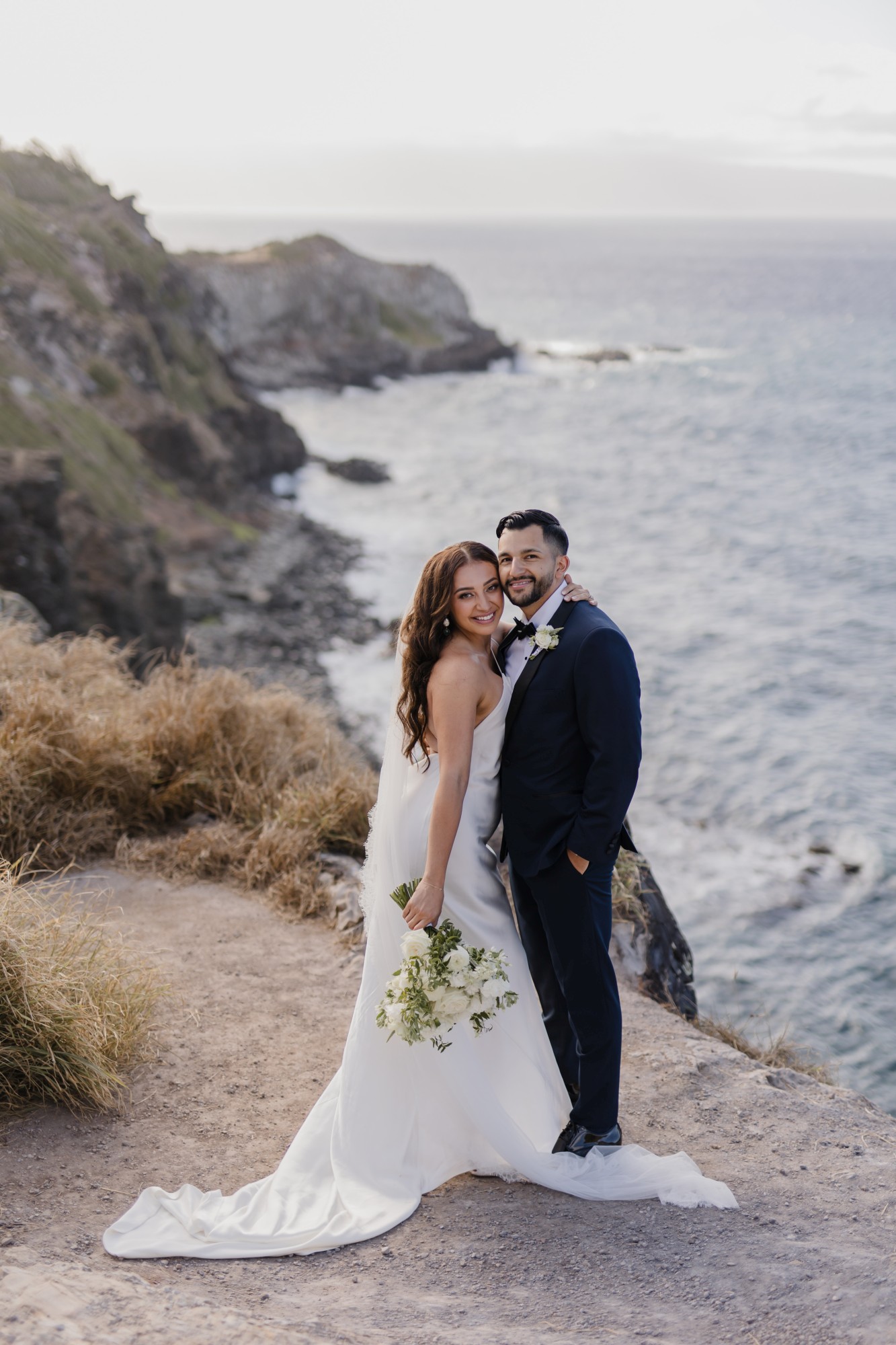 Natalie Jose - Roam Elopements Roam Elopements, Maui Elopements, Happy bride and groom embrace on a cliff overlooking the ocean.