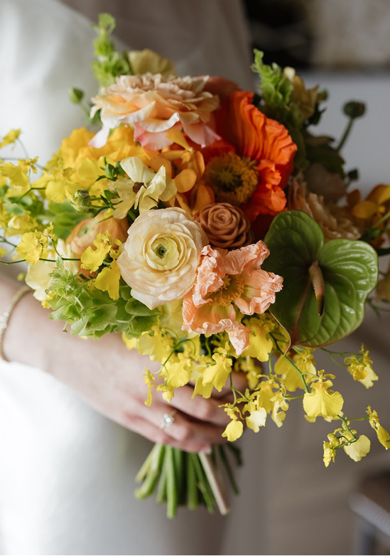 August-Dominic-Maui-Elopement-64 - Roam Elopements Colorful bouquet of yellow, orange, and cream flowers held by a person in a white dress.